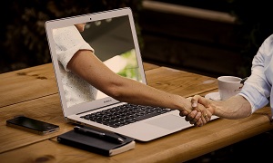 hand reaching out through the laptop for a handshake